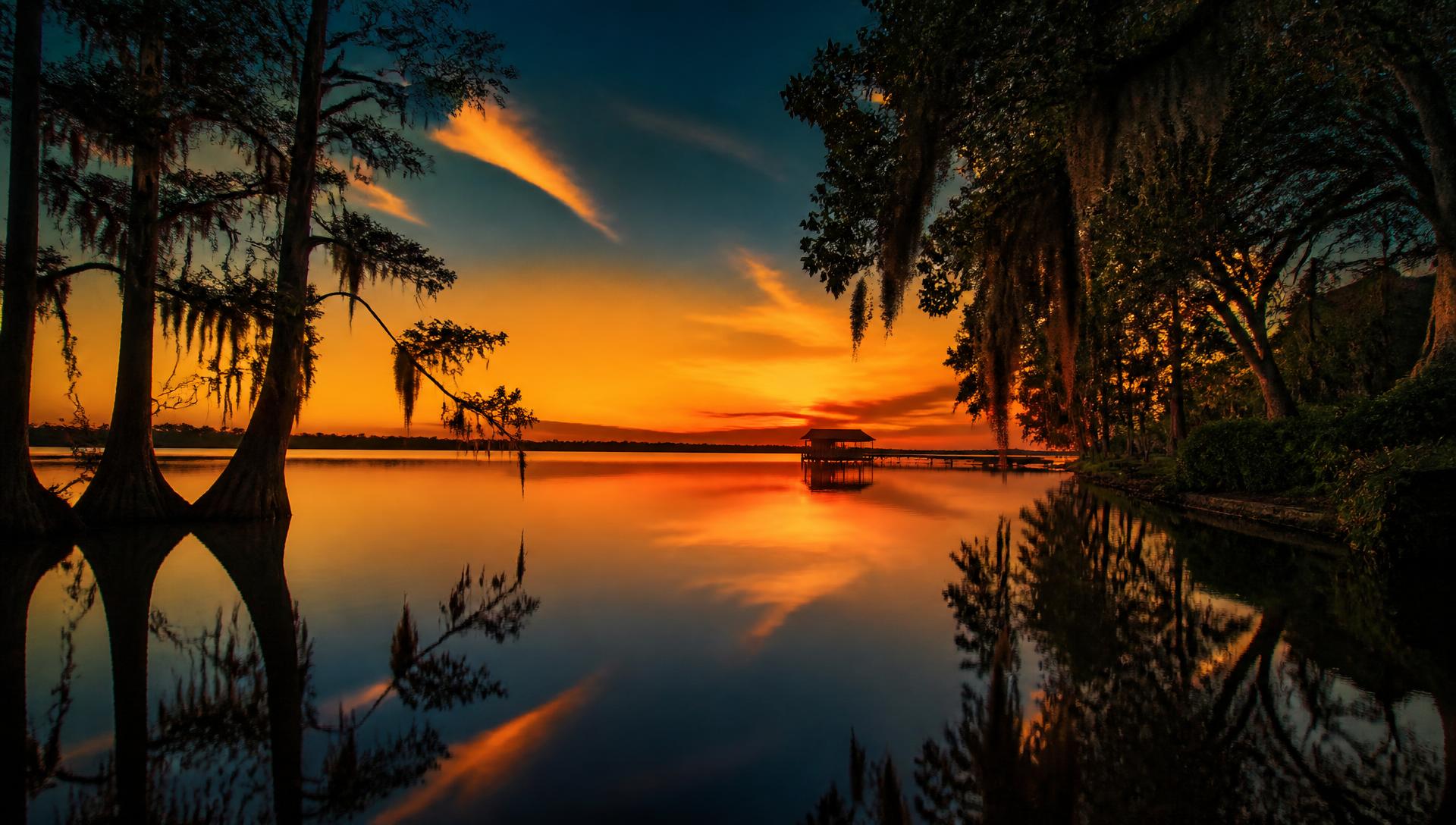 Sunset over a Windermere lake with silhouetted cypress trees and a distant dock